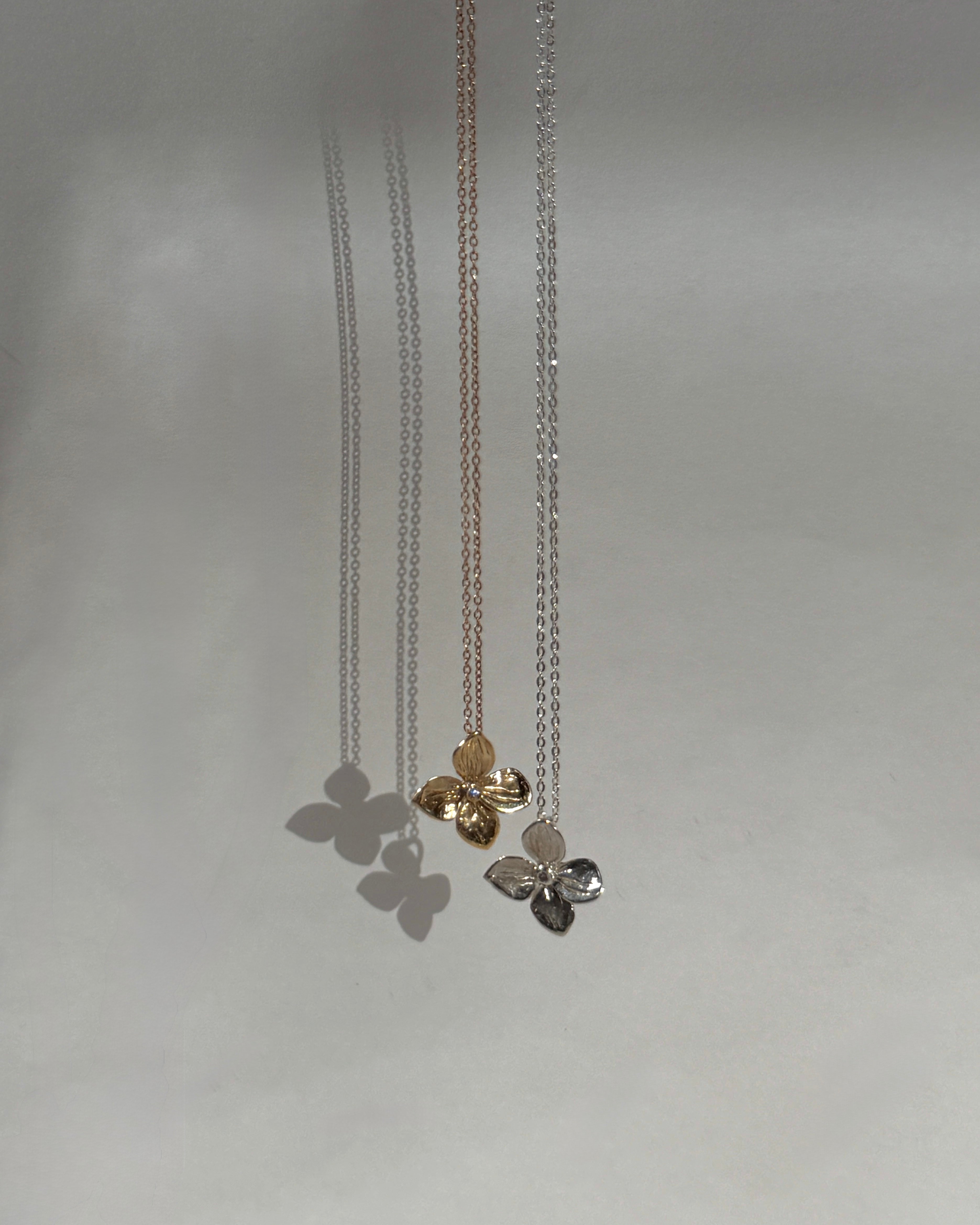 Gold and Silver Hydrangea pendants on thin gold chains against a light gray background